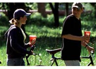 Coppia in bicicletta al parco con bicchieri carta di coca-cola